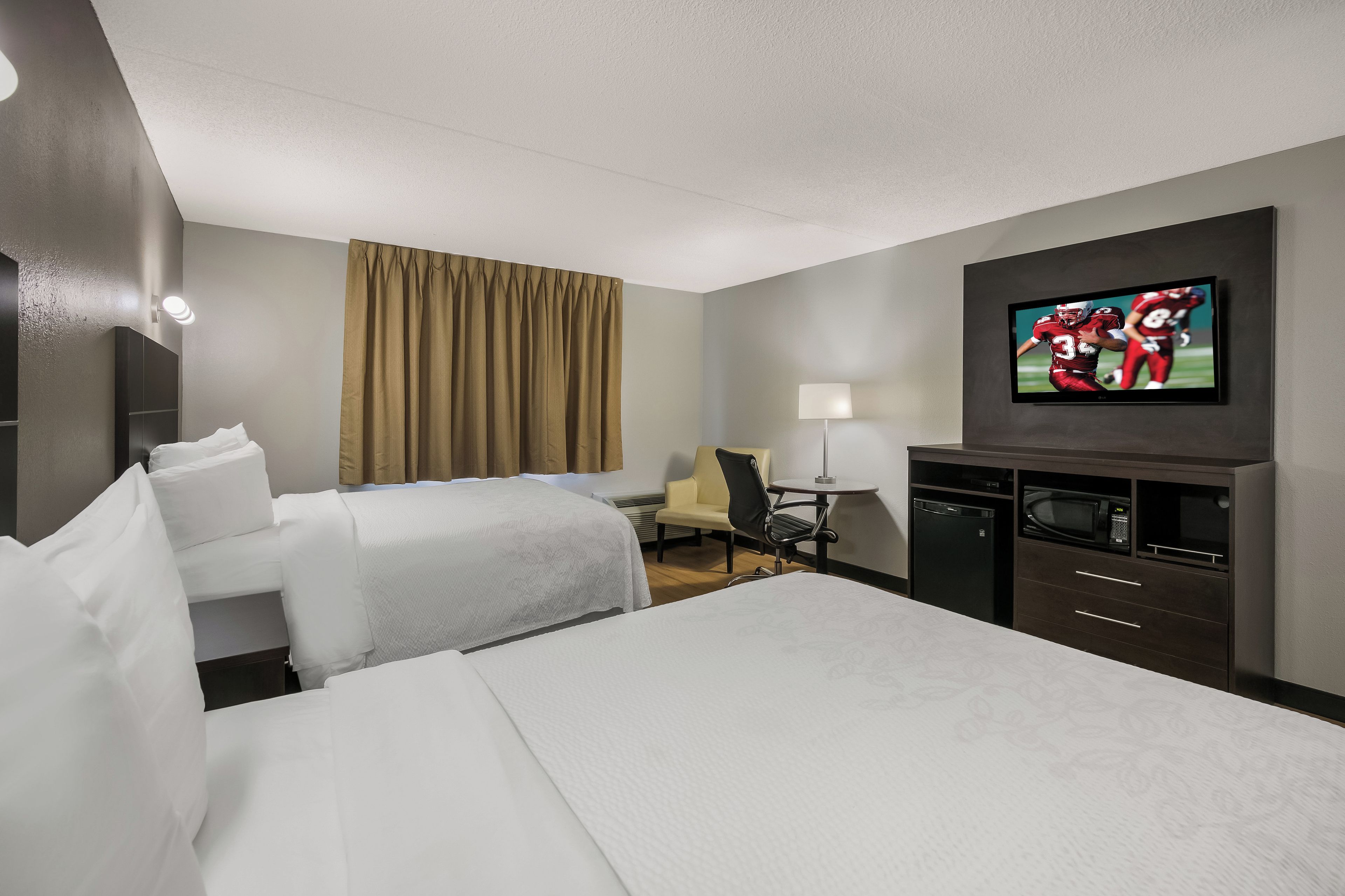 Habitación de hotel con dos camas, un escritorio, una silla, un televisor y un minibar.