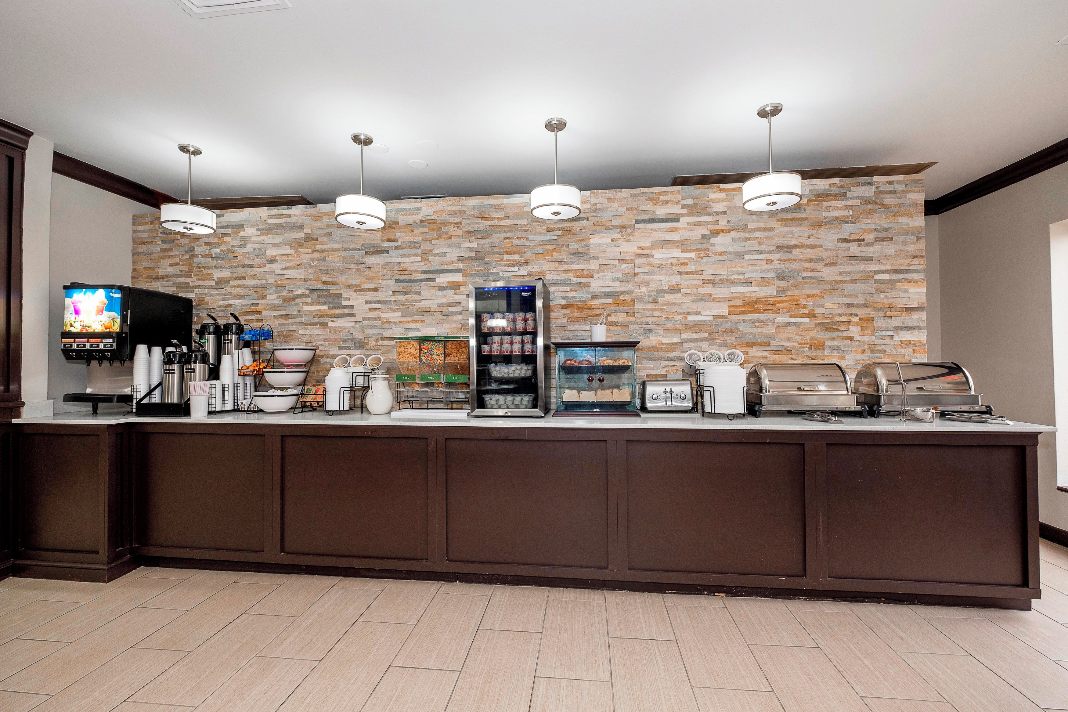 A breakfast bar with a stone wall backdrop, coffee machines, a TV, and a self-serve coffee station.