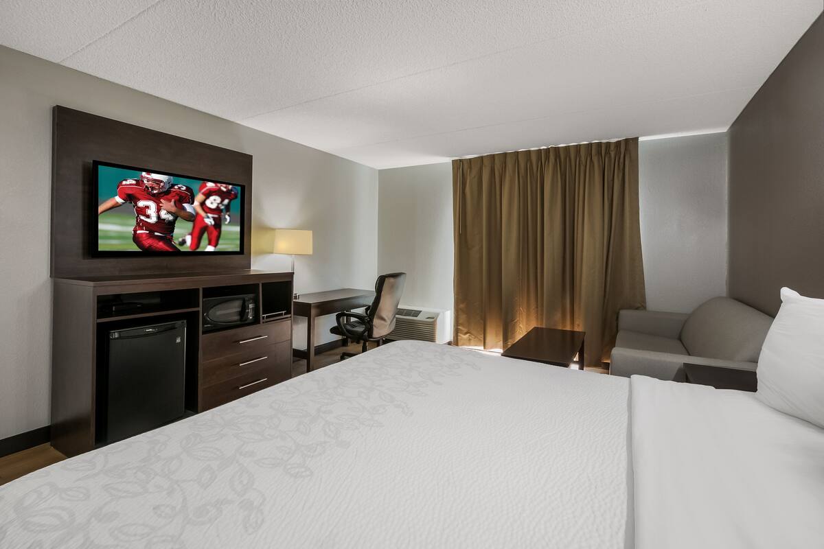 Ein Hotelzimmer mit einem großen Bett, einem Schreibtisch mit Stuhl, einem Fernseher und einer Minibar.
