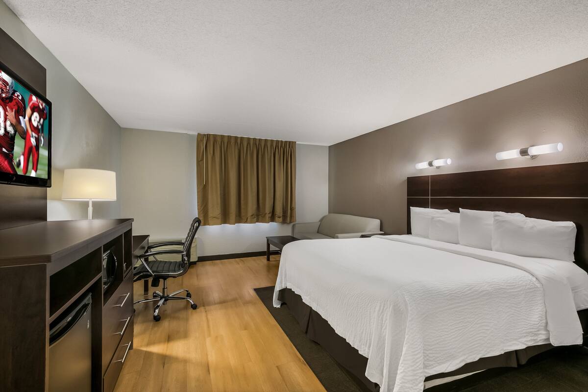 Ein Hotelzimmer mit Bett, Schreibtisch, Stuhl, Fernseher und Vorhängen.