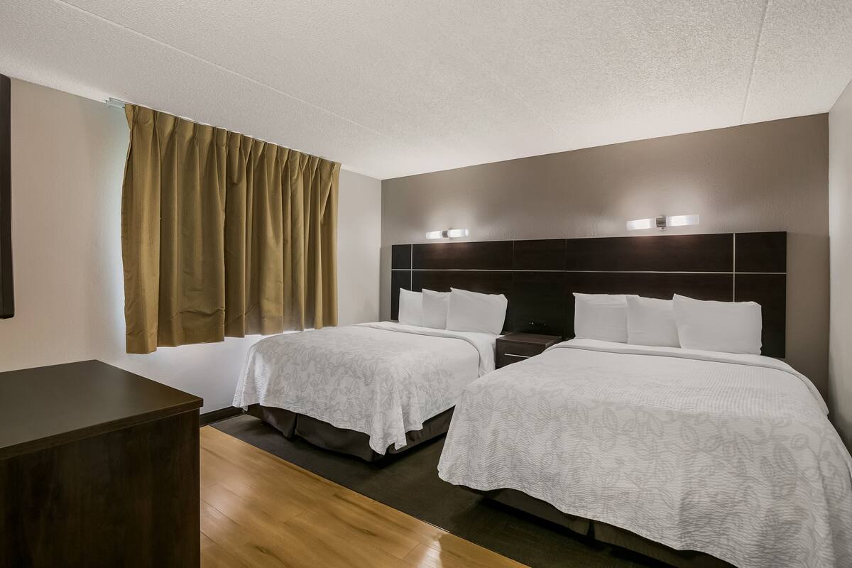 Ein Hotelzimmer mit zwei Betten, einem Holzschrank und einem großen Fenster mit Vorhängen.
