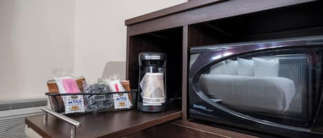 Un microondas y una cafetera sobre una encimera de madera, con una cesta que contiene infusiones y otros artículos.