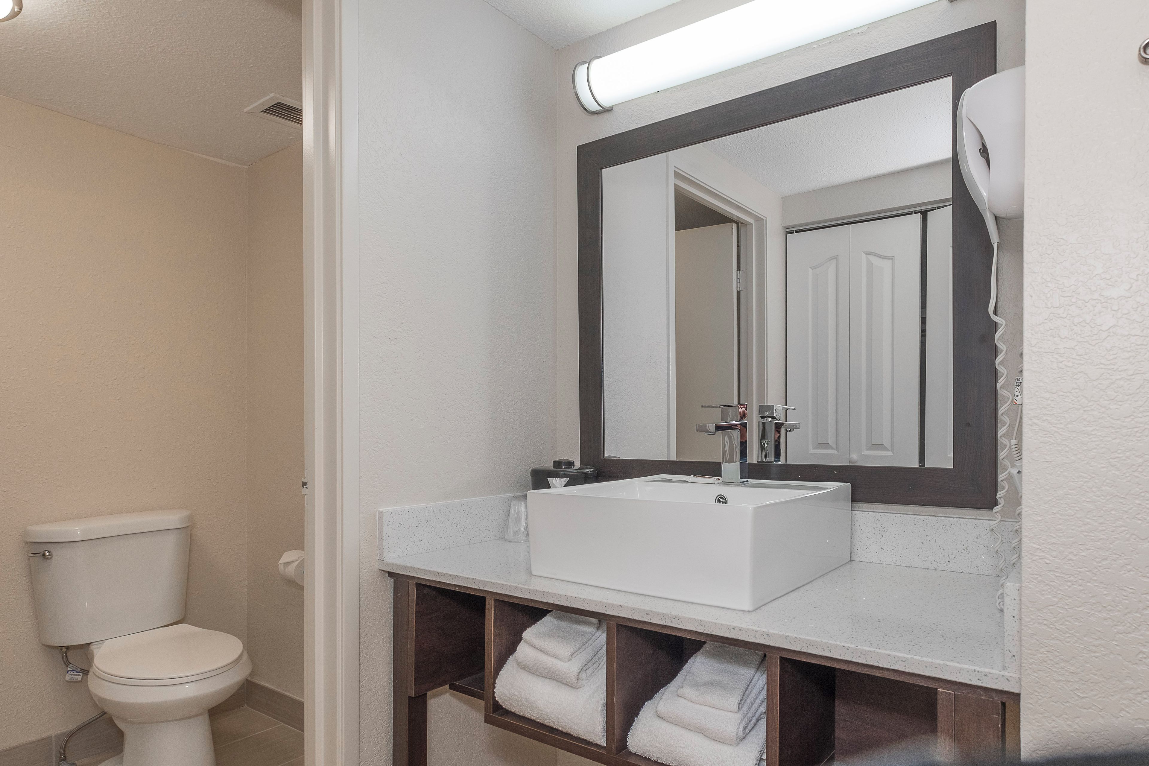 Un baño con inodoro blanco, lavamanos con espejo y toallero con toallas dobladas.