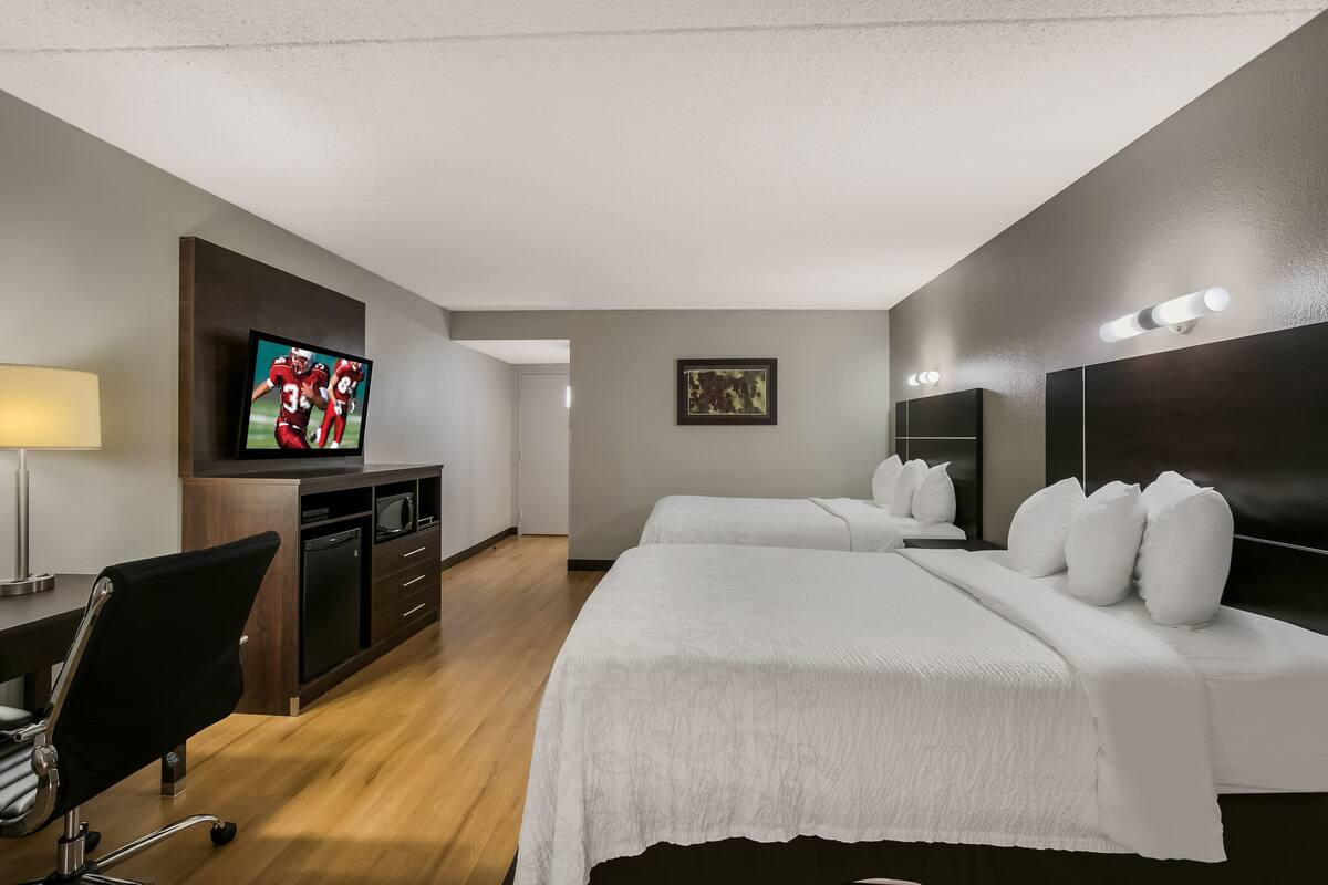Ein Hotelzimmer mit zwei Betten, einem Schreibtisch, einem Fernseher und einem Bild an der Wand.