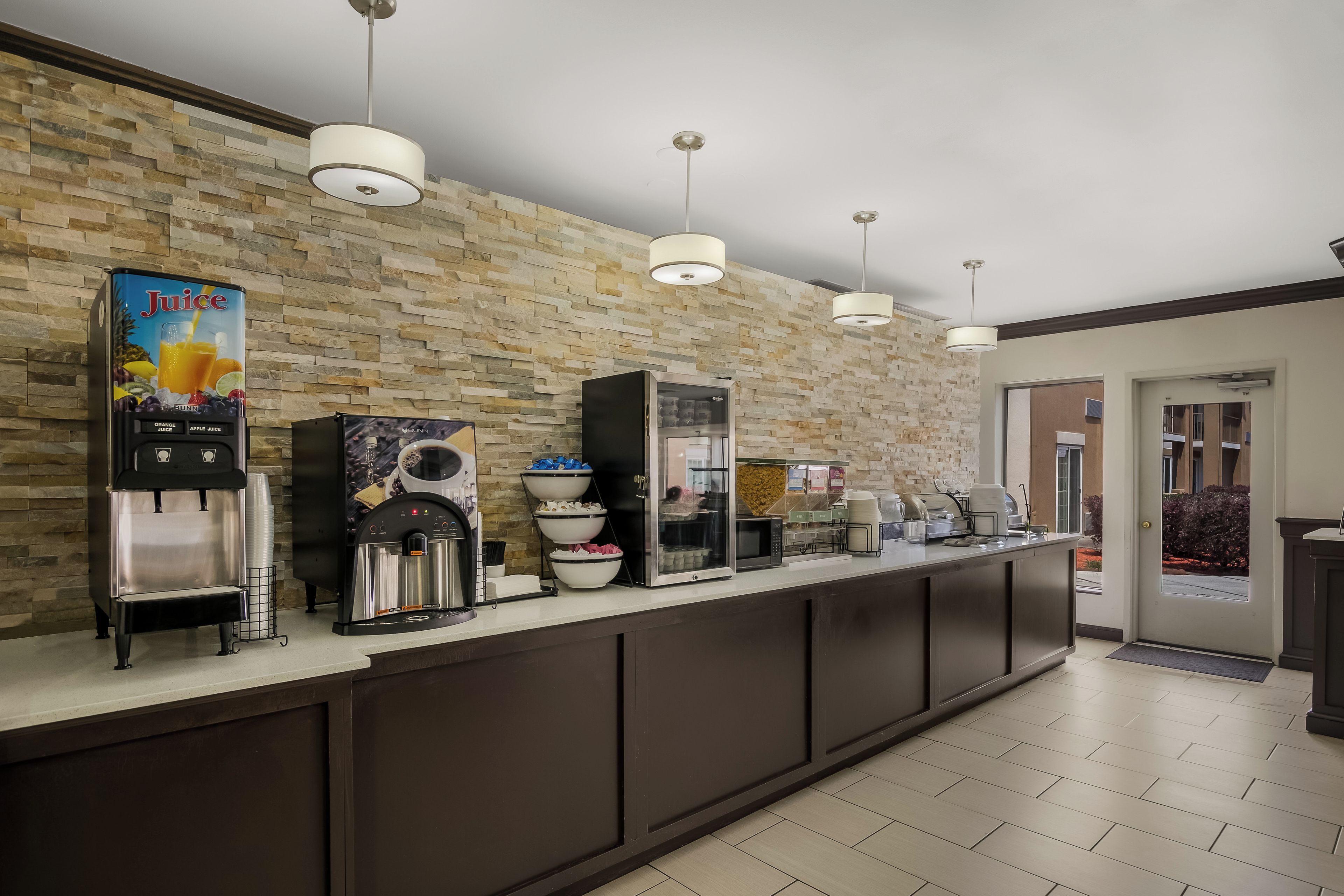 A modern kitchen area with a stone wall, a juice dispenser, a coffee machine, and a microwave.