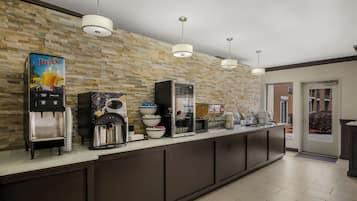 A modern kitchen area with a stone wall, a juice dispenser, a coffee machine, and a microwave.