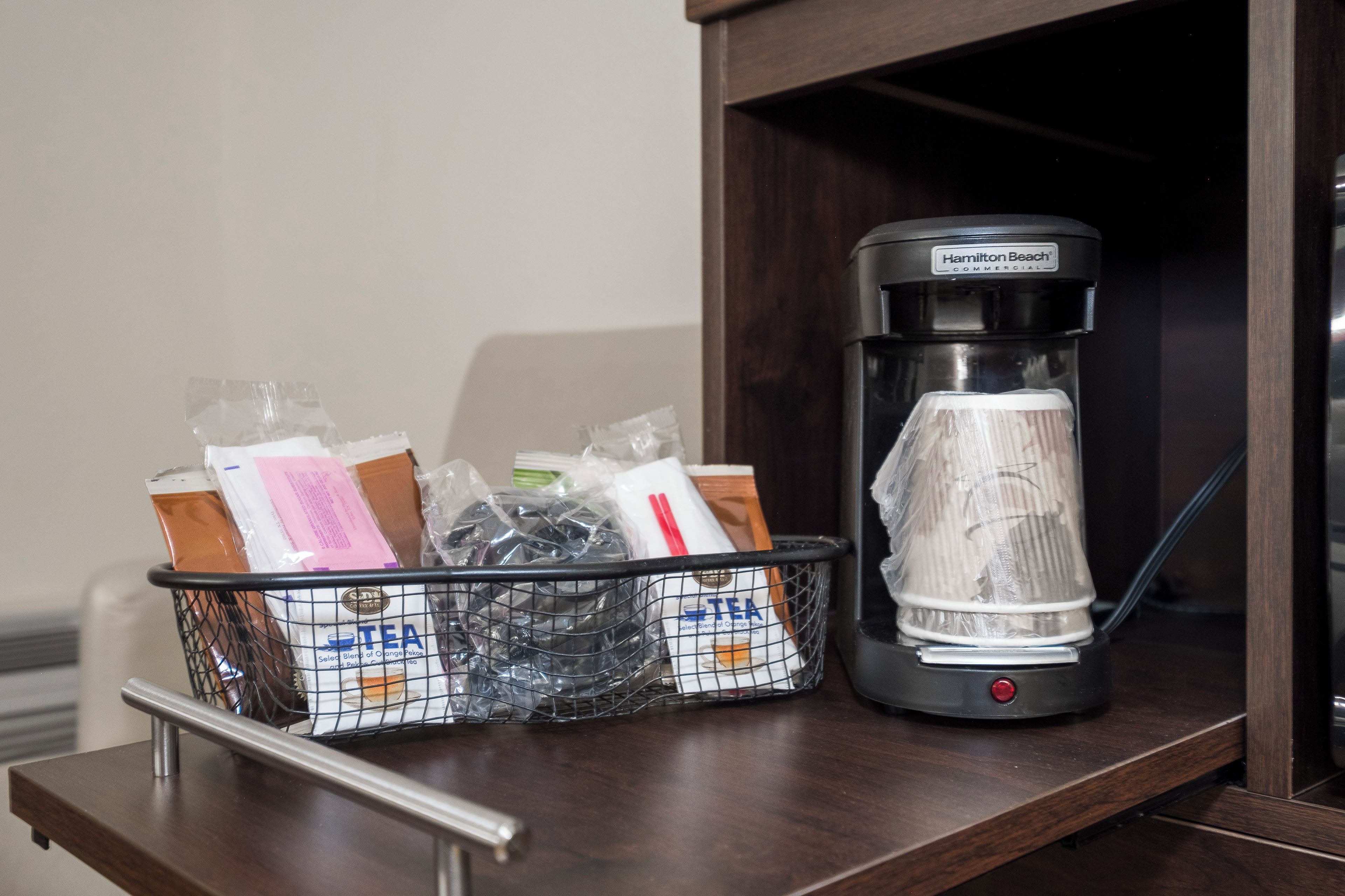 Una cafetera y un cesto de bolsitas de té sobre una encimera de madera.