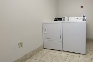 A laundry room with a front-loading washer and dryer, a power outlet, and a no-smoking sign on the wall. - Red Roof Inn PLUS+ & Suites Knoxville West-Cedar Bluff (Knoxville)