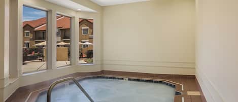 Un jacuzzi con escalera metálica, vista a una zona residencial a través de amplios ventanales y piso de baldosas.
