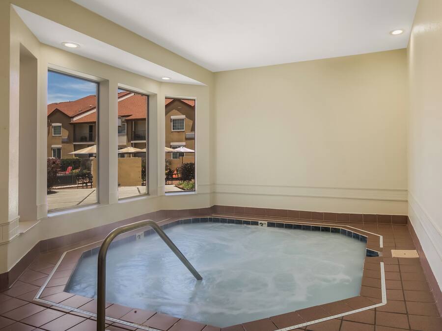 A hot tub with a metal ladder, a view of a residential area through large windows, and a tiled floor.