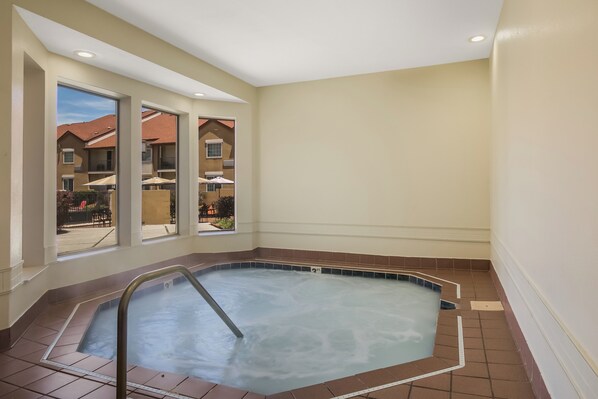 Un jacuzzi con escalera metálica, vista a una zona residencial a través de amplios ventanales y piso de baldosas.