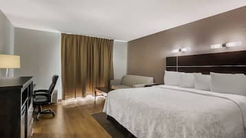 A hotel room with a large bed, a desk with a chair, a sofa, and a window with curtains.