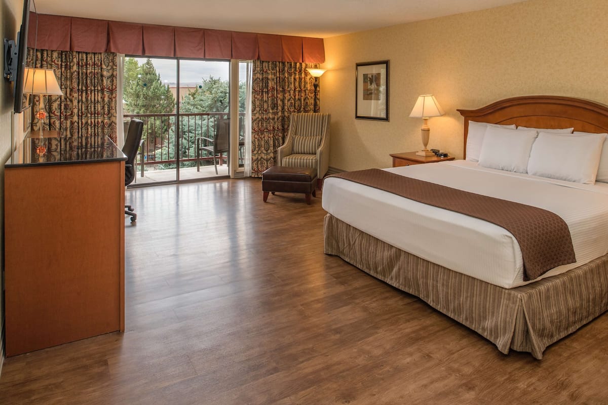 Habitación de hotel con una cama grande, un escritorio, una silla, una lámpara y vistas al exterior.
