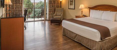 A hotel room with a large bed, a desk, a chair, a lamp, and a view of the outdoors.