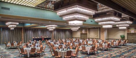 A banquet hall with round tables and chairs, chandeliers, and a patterned carpet.