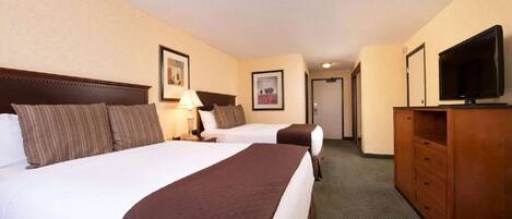 A hotel room with two beds, a television, a dresser, and a hallway leading to another room.