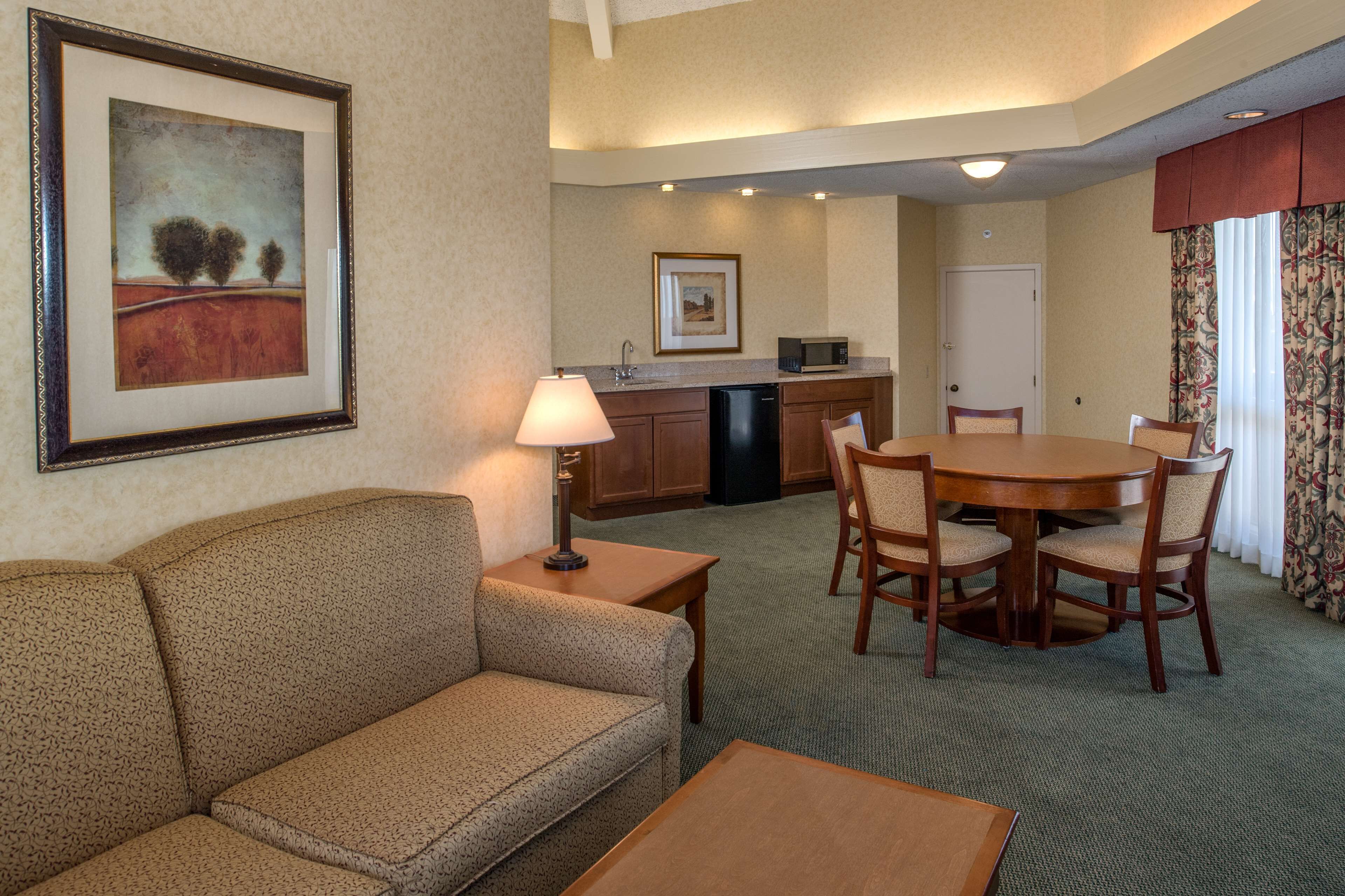Habitación de hotel con sofá, mesa de comedor, sillas, lámpara, microondas y lavabo.