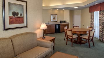 Habitación de hotel con sofá, mesa de comedor, sillas, lámpara, microondas y lavabo.
