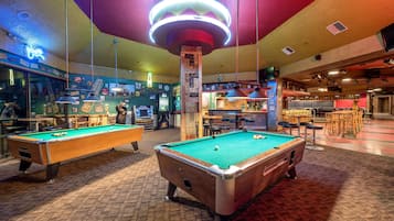 A pool table in a brightly lit room with a neon sign, a bar area, and various seating arrangements.