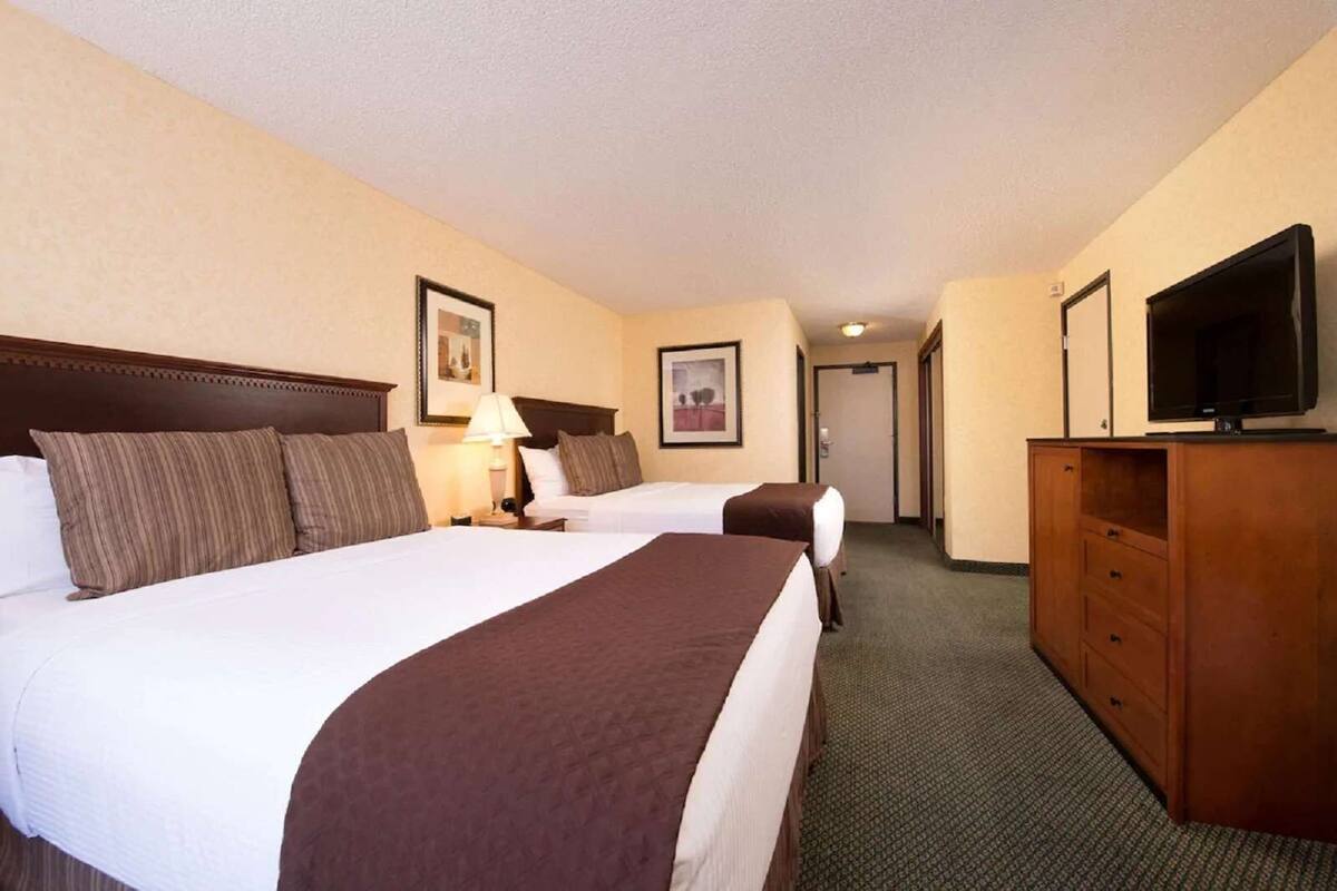 Habitación de hotel con dos camas, televisión, cómoda y un pasillo que conduce a otra habitación.