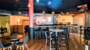 Un área de bar moderna con suelo de madera, distintas opciones de asientos como mesas redondas y taburetes, y varios candelabros colgantes.