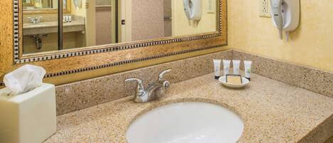 Une salle de bain dotée d’un comptoir en granit, d’un lavabo, d’un miroir et de deux sèche-cheveux fixés au mur.