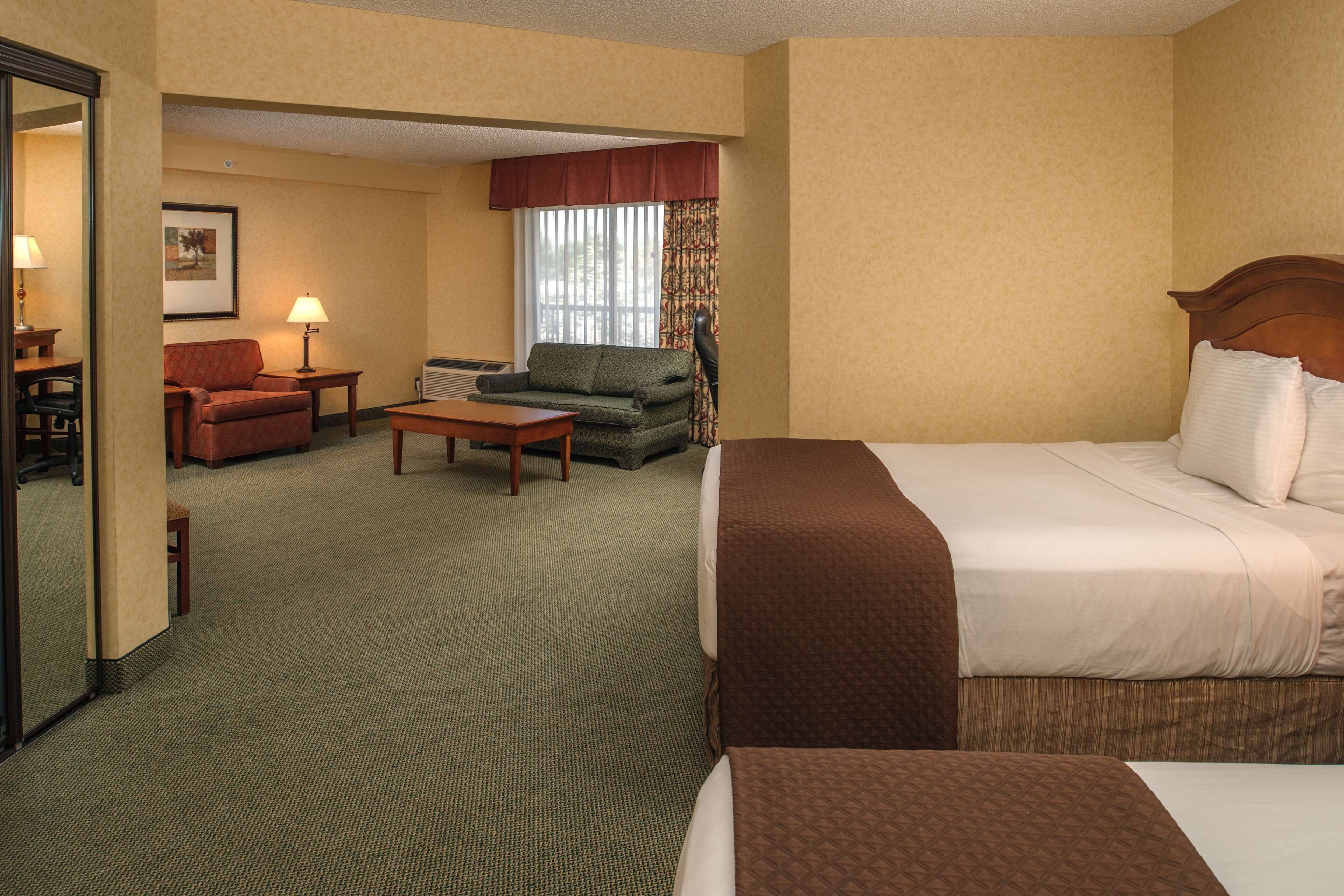 Habitación de hotel con cama, sofá, silla, mesita y ventana con cortinas.