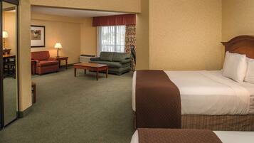 Habitación de hotel con cama, sofá, silla, mesita y ventana con cortinas.