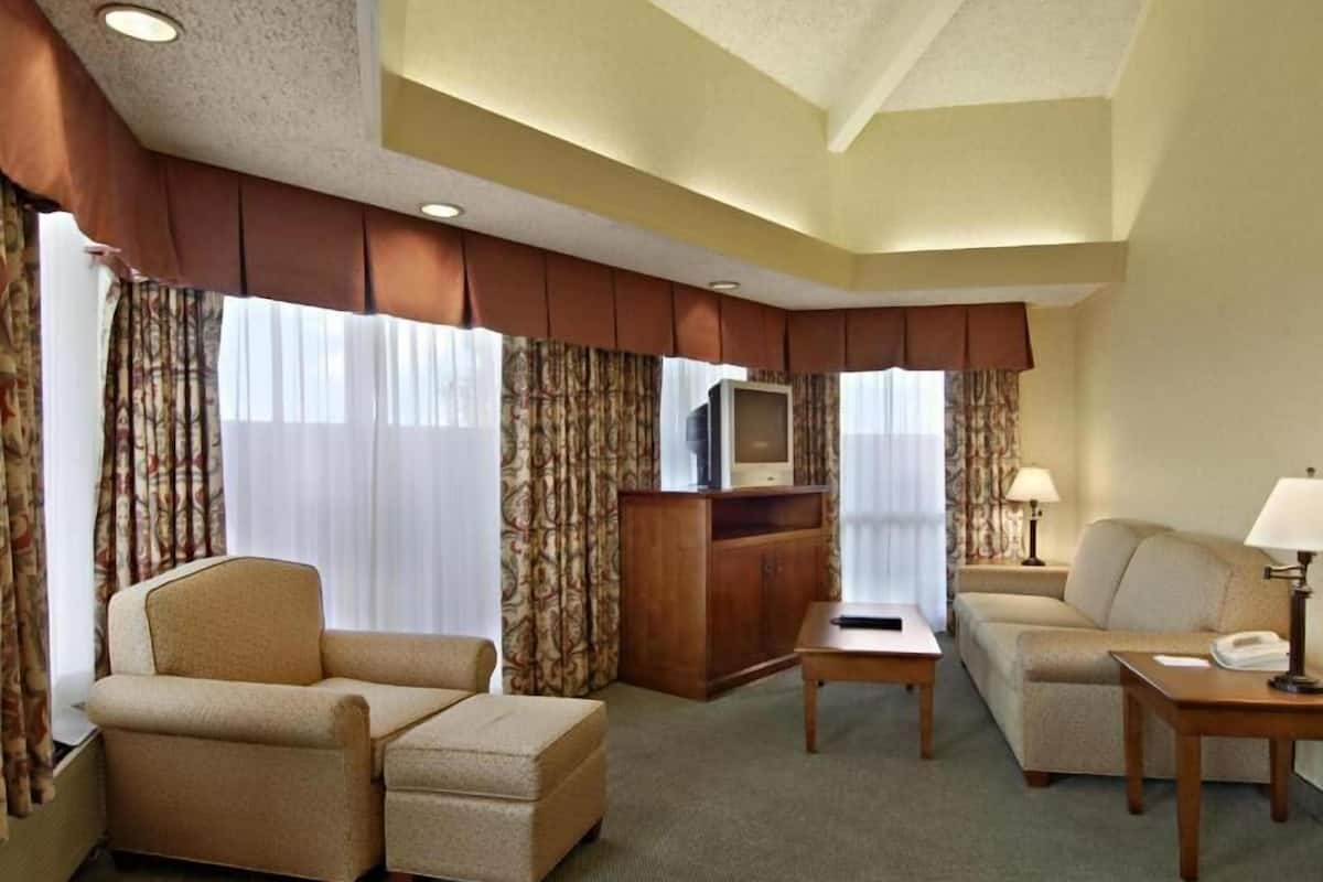 Habitación de hotel con sofá, sillón, reposapiés, mueble para televisión y lámparas.