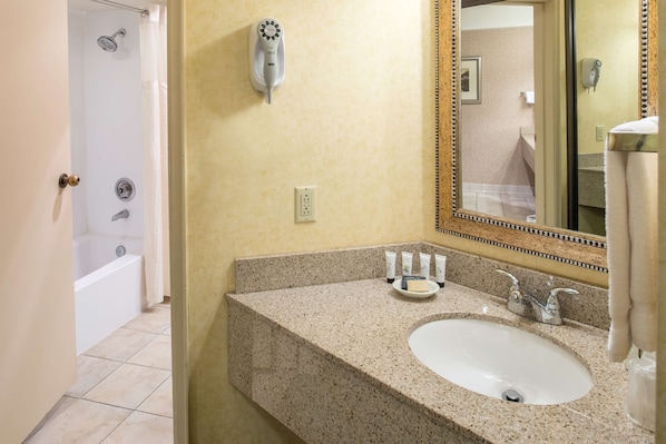 A bathroom with a granite countertop, a sink, a mirror, a handheld showerhead, and a bathtub.