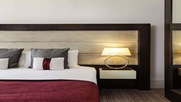 A hotel room with a large bed, a bedside table with a lamp, and a mirror on the wall.