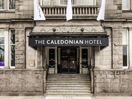 La entrada del Hotel Caledonian, con un letrero negro, fachada de piedra y un conjunto de escalones que conducen a la entrada.