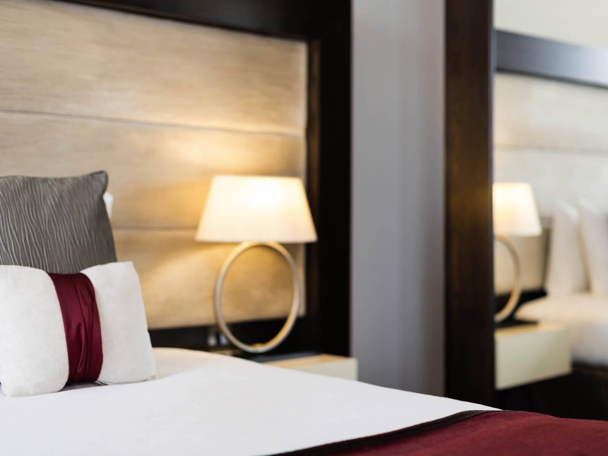 Habitació d'hotel amb un llit ben fet, una làmpada de nit i un mirall que reflecteix la làmpada.