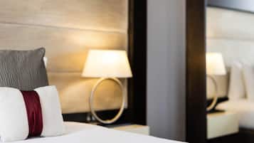 Ein Hotelzimmer mit einem ordentlich bezogenen Bett, einer Nachttischlampe und einem Spiegel, der die Lampe reflektiert.
