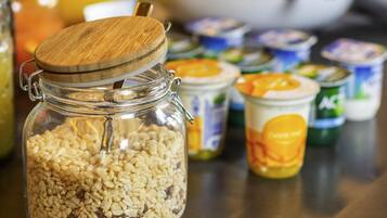 Ein durchsichtiges Glasgefäß mit Holzdeckel, gefüllt mit Cornflakes, umgeben von verschiedenen Lebensmitteln.