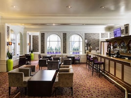 Un hall de hotel con bar, zona de estar, grandes ventanales de arco y alfombra estampada.