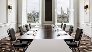 Sala de conferência com uma mesa comprida, cadeiras e grandes janelas com vista para a cidade.