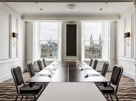 Un salón de conferencias con una mesa larga, sillas y ventanas amplias que dan a vistas de la ciudad.