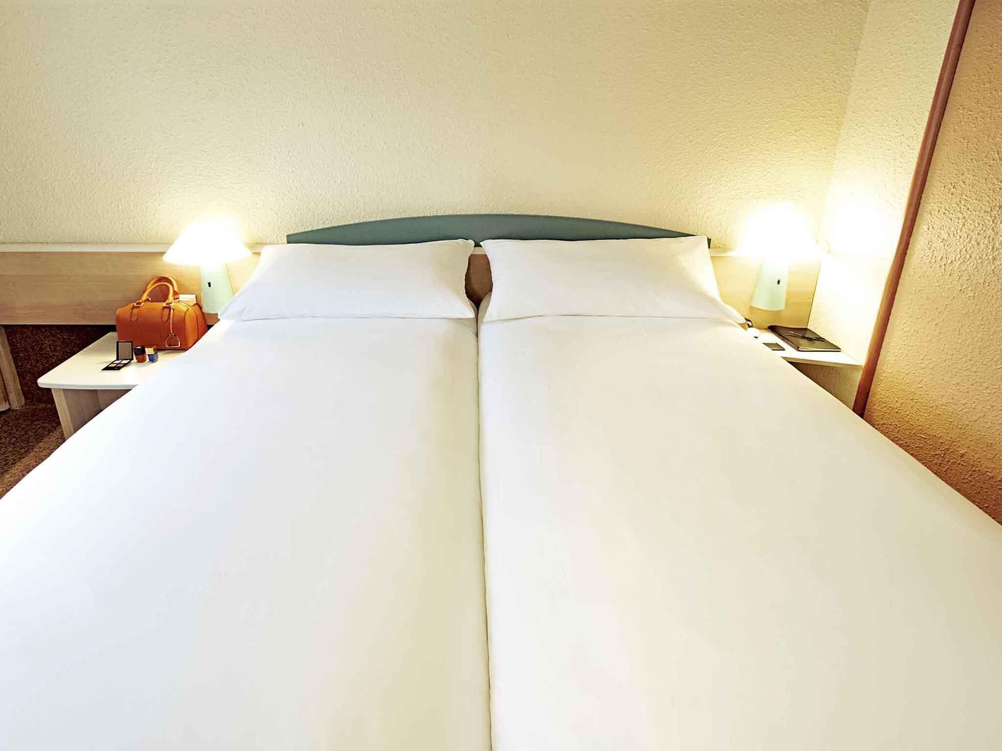 A hotel room with a single bed, two bedside tables, and a nightstand with a lamp.