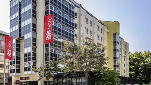 A modern hotel building with multiple floors, large windows, and red signage indicating it is an ibis hotel. - ibis Augsburg Hauptbahnhof (Augsburg)