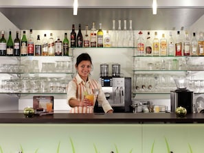 A bar area with a bartender, shelves of liquor bottles, and a coffee machine. - ibis Augsburg Hauptbahnhof (Augsburg)