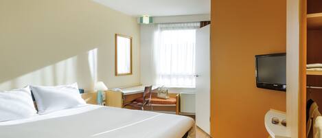 Habitación de hotel con una cama grande, un escritorio con silla, un televisor montado en la pared y una ventana con cortinas.