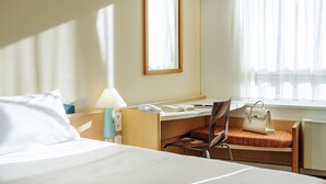 A hotel room with a bed, a desk with a chair, a lamp, a handbag, and a window with curtains. - ibis Augsburg Hauptbahnhof (Augsburg)