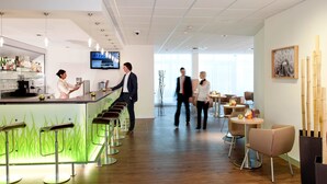 A modern bar area with a long counter, bar stools, and a television screen. - ibis Augsburg Hauptbahnhof (Augsburg)