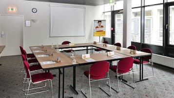 A conference room with a large table, red chairs, a whiteboard, and a window with a city view.