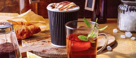 Una mesa con una taza de té, un croissant, una cafetera y un tarro de azúcar.