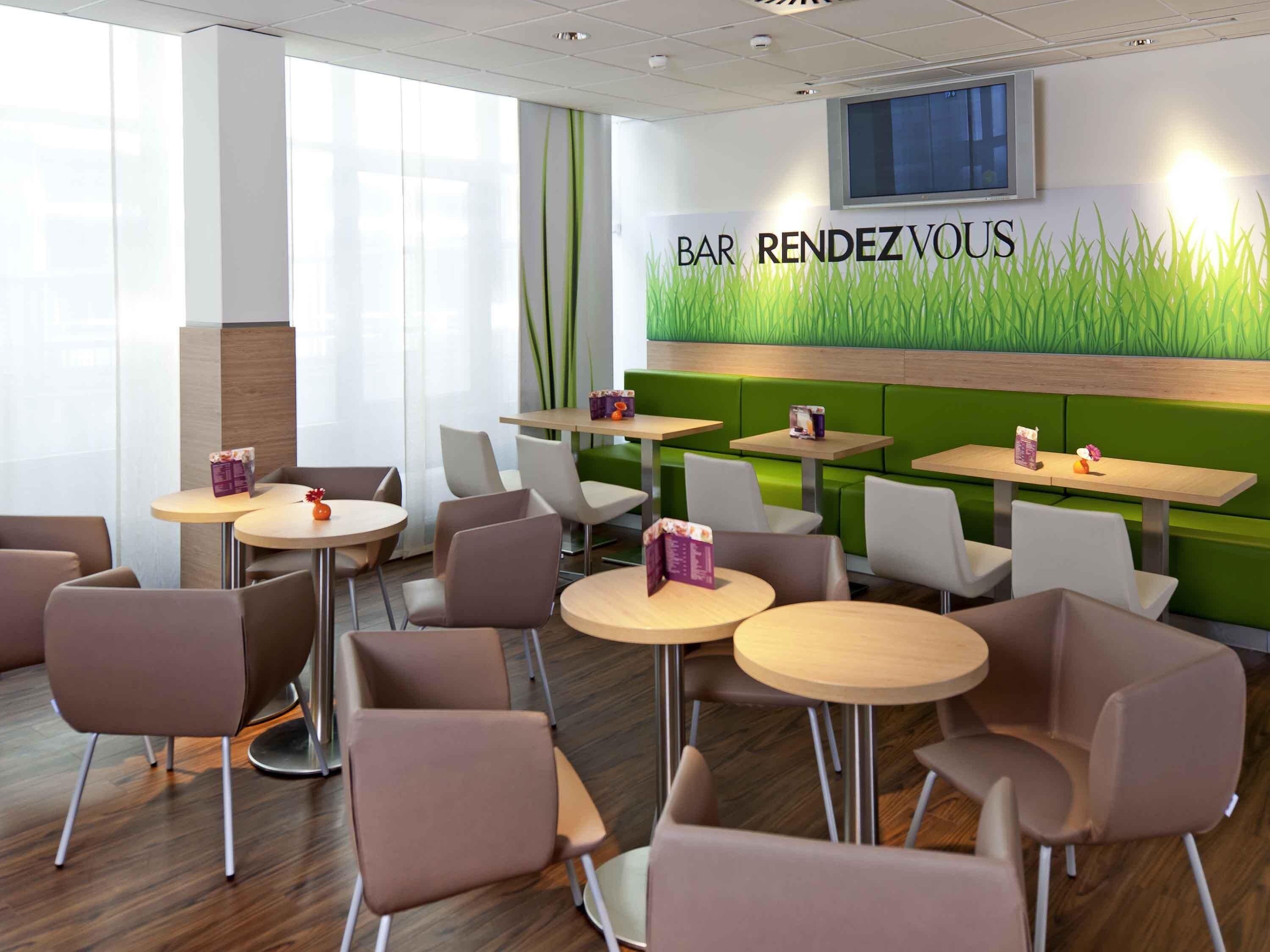 Ein modernes Restaurant mit grünen Sitzbänken, runden Tischen und einem an der Wand befestigten Fernseher.