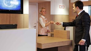 A hotel reception area with a wooden reception desk, a television mounted on the wall, and a sign indicating room number BMZ. - ibis Augsburg Hauptbahnhof (Augsburg)