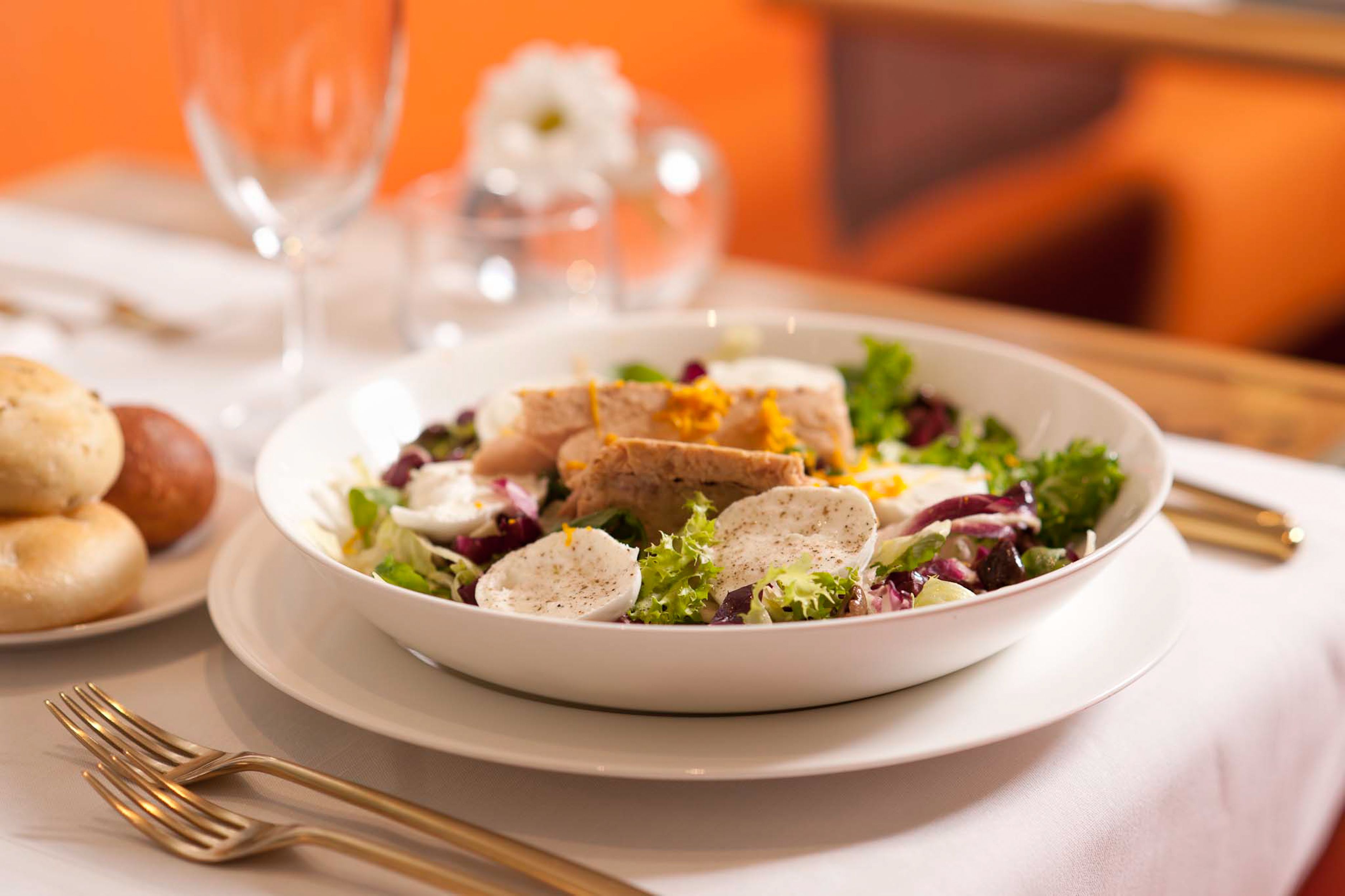 A dining table with a white plate containing a salad, bread, and a glass of water.