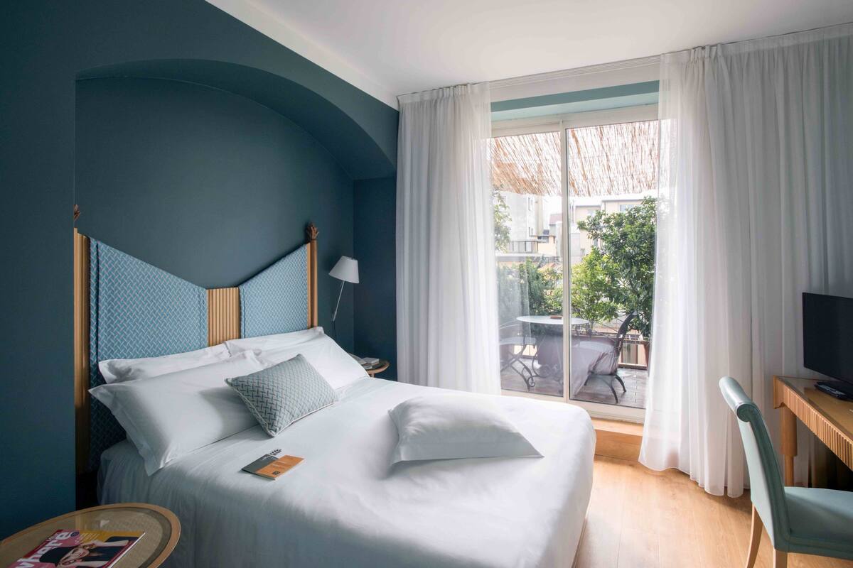 A hotel room with a bed, a desk, a chair, and a view of the outside.
